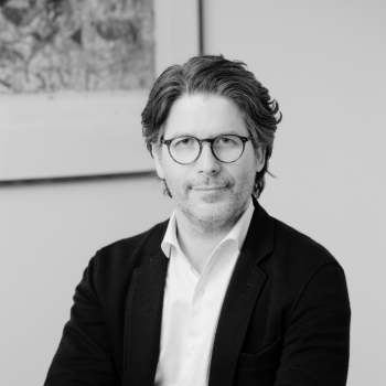 Black-and-white portrait of a man with glasses and wavy hair wearing a blazer.